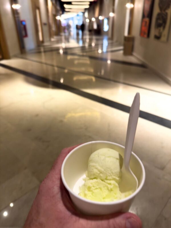 Hand holding a small cup of vanilla gelato with a white spoon in a softly lit hallway at AVA Resort Cancun.