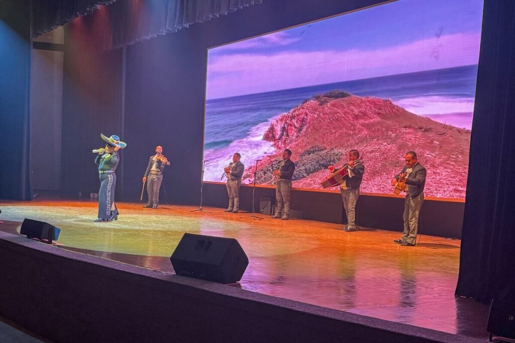 Live performance at AVA Resort Cancun with a singer in traditional attire and a mariachi band on stage in front of a large screen backdrop.